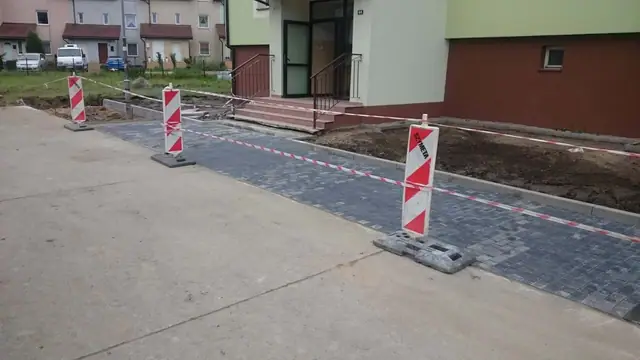 Świeżo ułożony chodnik z kostki brukowej odgrodzony słupkami ostrzegawczymi przy budynkach
