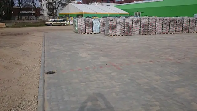 Fragment gotowej kostki parkingowej obok spaletowanych materiałów budowlanych