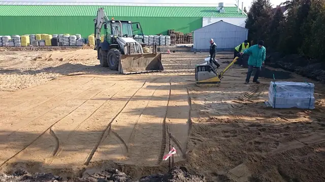 Ekipa rozkłada geowłókninę na piaszczystym terenie pod przyszły parking