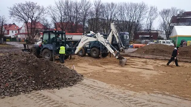 Koparka i cysterna pracują na piaszczystym placu budowy parkingu