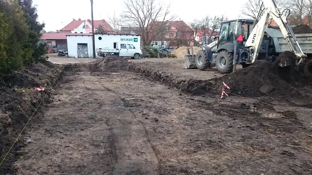 Koparka wyrównuje ziemię, widoczne ślady kół na rozjeżdżonym terenie