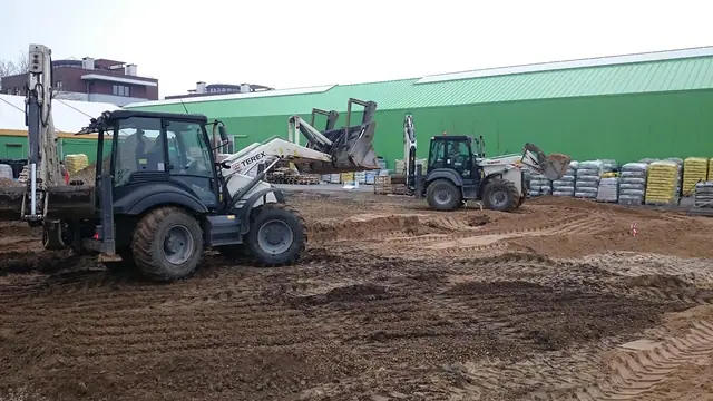 Dwie koparko-ładowarki wyrównują teren pod nawierzchnię parkingu